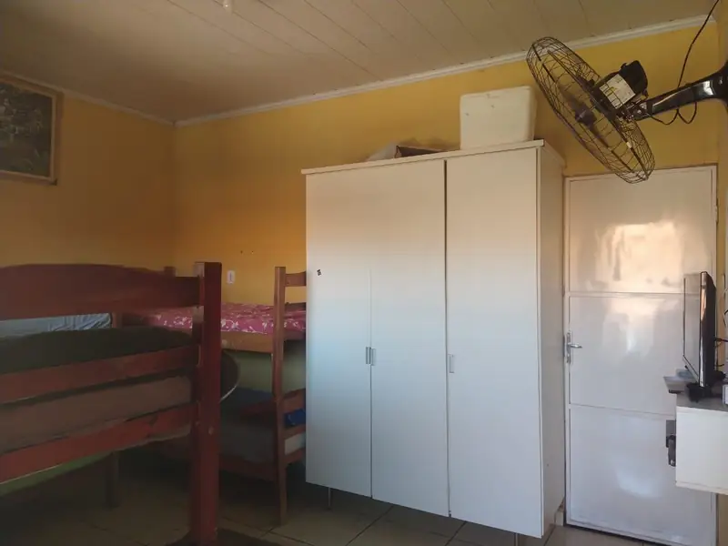 Dormitório com beliches de madeira, guarda-roupa branco e ventilador de parede