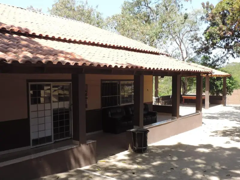 Varanda coberta com sofás e mesa de sinuca, ao lado de um pátio sombreado por árvores